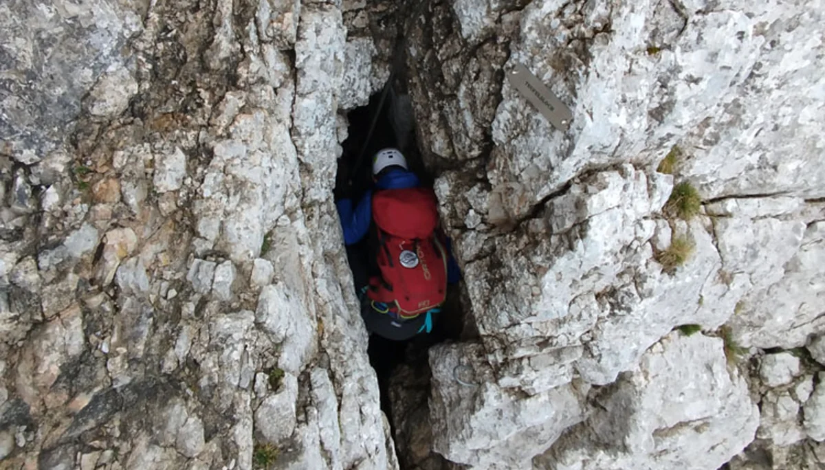 Person mit rotem Rucksack und Helm klettert durch eine schmale Felsspalte im Gebirge | © Florian Ludwig