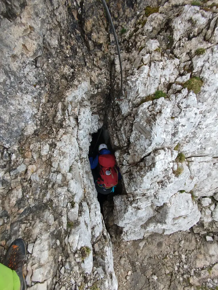 Person mit rotem Rucksack und Helm klettert durch eine schmale Felsspalte im Gebirge | © Florian Ludwig