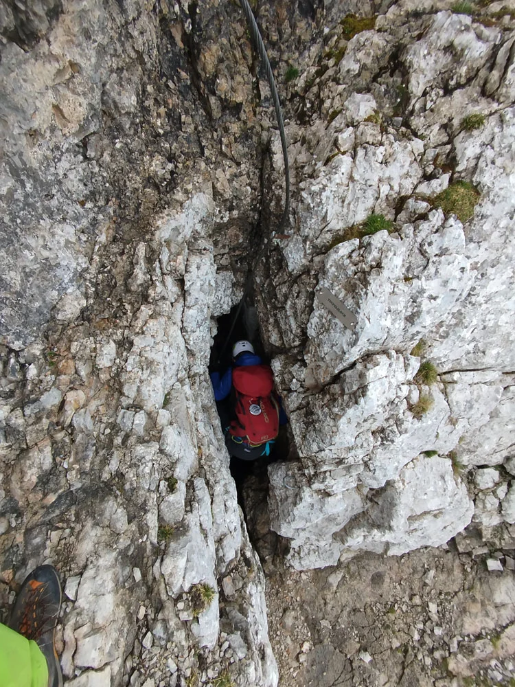 Person mit rotem Rucksack und Helm klettert durch eine schmale Felsspalte im Gebirge | © Florian Ludwig