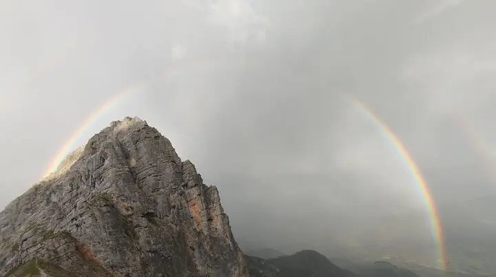 Regenbogen über einem felsigen Berggipfel mit bewölktem Himmel | © Florian Ludwig