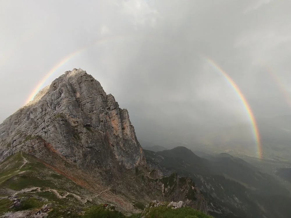 Regenbogen über einem felsigen Berggipfel mit bewölktem Himmel | © Florian Ludwig