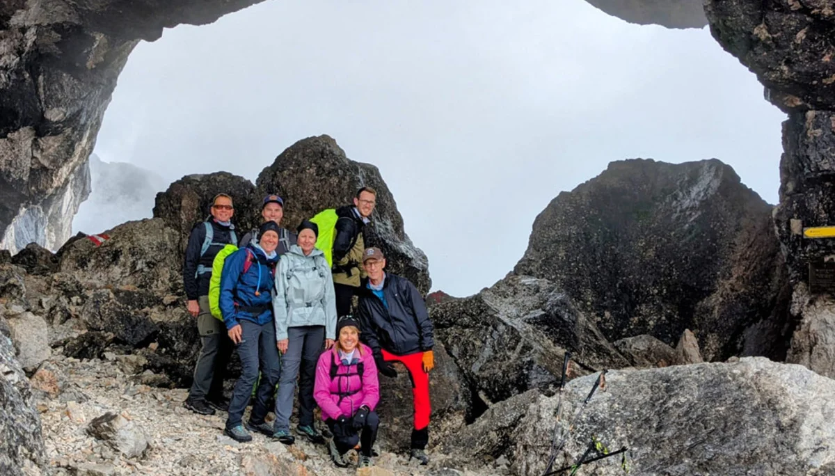 Sieben Personen in Outdoor-Bekleidung posieren in einer Felsformation mit großer Öffnung und Nebel im Hintergrund | © Florian Ludwig