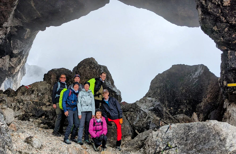 Sieben Personen in Outdoor-Bekleidung posieren in einer Felsformation mit großer Öffnung und Nebel im Hintergrund | © Florian Ludwig