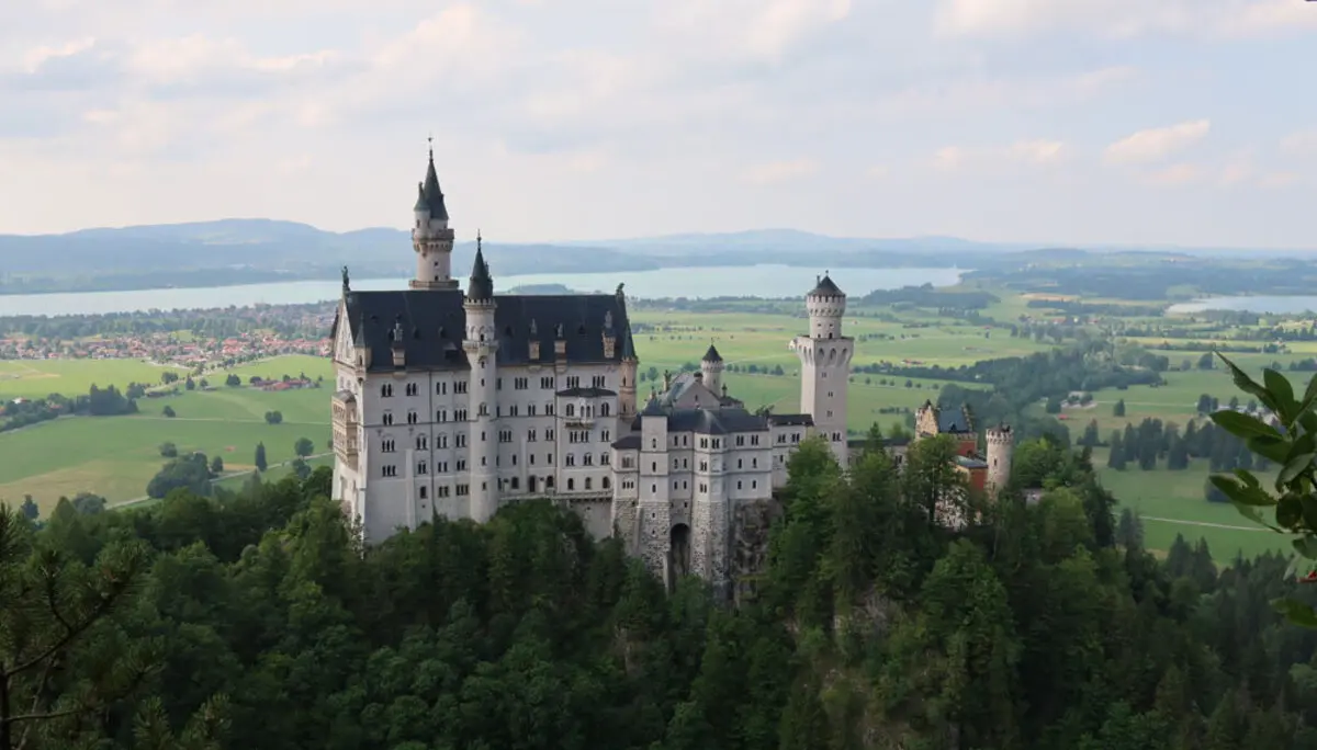 Schloss Neuschwanstein auf bewaldetem Hügel mit Blick auf Seen und grüne Landschaft im Hintergrund | © Christian Stadtmüller
